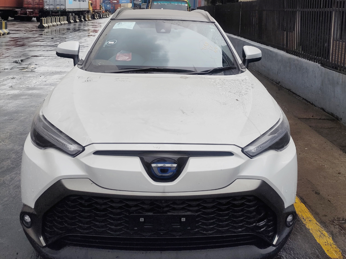 Car-Planet A white compact crossover SUV with a distinctive front grille and sharp LED headlights, parked on a wet pavement near a line of shipping containers. The vehicle features a blue emblem at the center of the grille.