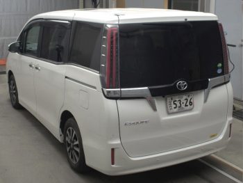 A luxurious 2019 Toyota Esquire Gi minivan in pristine white is parked indoors. The vehicle features a sleek and modern design, with a prominent chrome grille and sharp, sophisticated headlights. The minivan's clean lines and spacious body are accentuated by large windows and stylish alloy wheels, giving it an elegant and upscale appearance. The license plate and a small "JU" logo are visible, indicating it is from a Japanese auction.